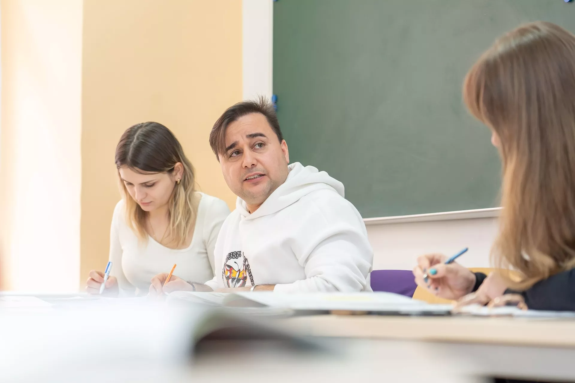 Ein Mann und eine Frau sitzen an einem Schreibtisch vor einer Tafel